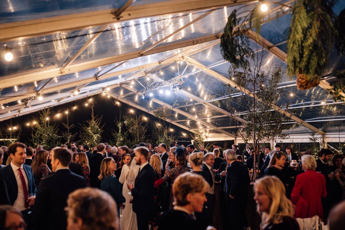 Large clear tent with guests and sky showing through the roof