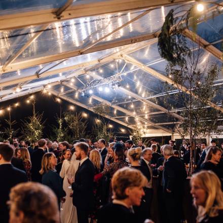 Large clear tent with guests and sky showing through the roof
