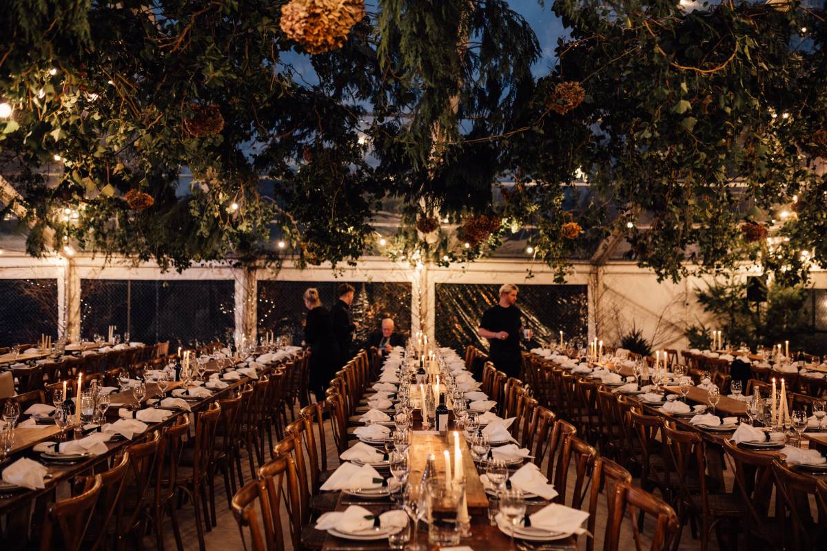 Dark wood rustic tables laid up under hanging foliage and festoon lighting