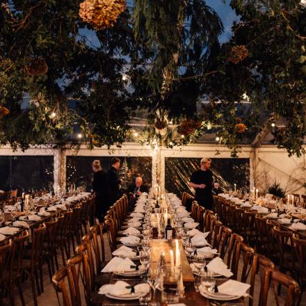 Dark wood rustic tables laid up under hanging foliage and festoon lighting