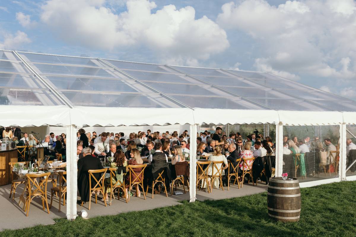 Seated guests in a open sided transparent wedding marquee