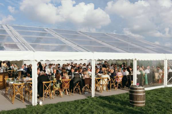 Seated guests in a open sided transparent wedding marquee