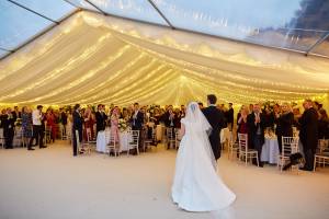 Bride and groom entering a marquee with a fairy light canopy covering the dining section, and another section with clear roofs