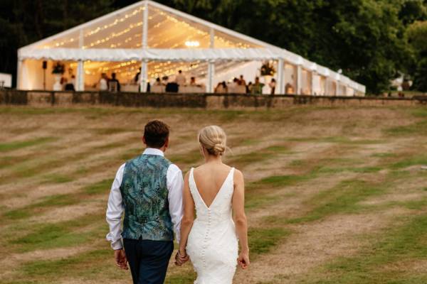 Bride and groom walk towards their partially transparent marquee