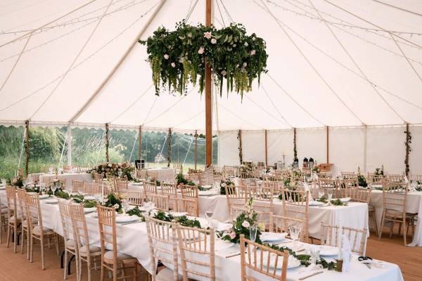 Pretty, light wedding reception with flowers and chiavari chairs inside traditional tent